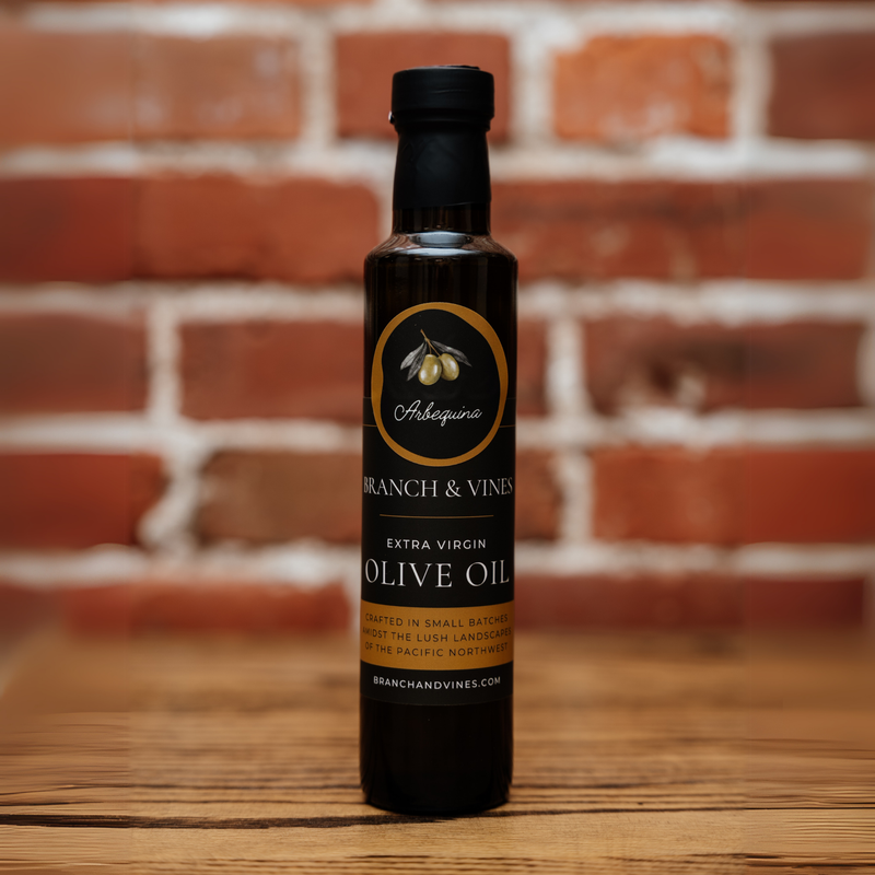 A bottle of Arbequina Extra Virgin Olive Oil placed in front of a warm, rustic brick backdrop, evoking an artisanal and natural feel.