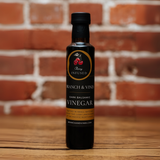 A bottle of Black Cherry Balsamic Vinegar set against a textured brick background, exuding artisanal sophistication and charm.