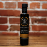 Hickory Smoked Dark Balsamic Vinegar bottle against a rustic brick wall.